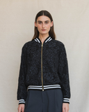 Person wearing a navy lace jacket with white and black accents on a plain background