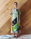 Model wearing a long patchwork dress against a wooden wall.