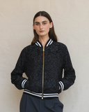 Person wearing a navy lace jacket with white and black accents on a plain background