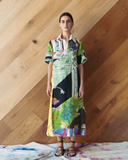 Model wearing a colorful dress with abstract patterns against a wooden wall.