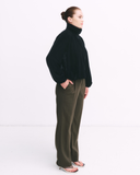 Person wearing a black funnel neck and olive green pants on a white background