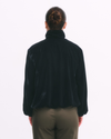 Person wearing a black turtleneck jacket and olive pants on a white background