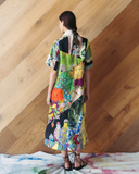 Woman wearing a colorful patchwork dress against a wooden wall.