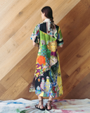 Model wearing a long patchwork dress against a wooden wall.