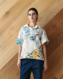 Model wearing a colourful, patchwork polo shirt against a wooden wall.