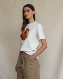 Model wearing a white t-shirt with a colourful floral design against a beige background