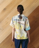 Model wearing a colourful, patchwork polo shirt against a wooden wall.