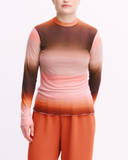 Person wearing a long-sleeve top with a gradient from brown to pink on a white background