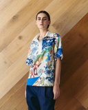 Model wearing patchwork Polo Top - mixed print shirt against a wooden wall.