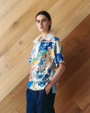 Model wearing patchwork Polo Top - mixed print shirt against a wooden wall.