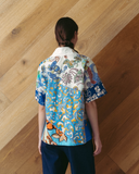 Model wearing patchwork Polo Top - mixed print shirt against a wooden wall.
