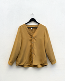 gold blouse hanging up against a white wall