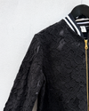 Black lace jacket with a gold zipper on a hanger against a white wall