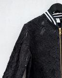 Black lace jacket with a gold zipper on a hanger against a white wall