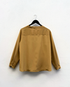 gold blouse hanging up against a white wall