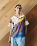 Model wearing a colourful geometric-patterned shirt against a wooden wall.