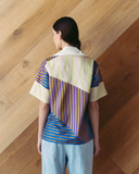 Model wearing a colourful geometric-patterned shirt against a wooden wall.