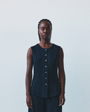 Woman wearing a dark blue sleeveless top with buttons against a plain background
