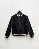 Black bomber jacket with white trim on a hanger against a white background