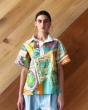 Model wearing patchwork Polo Top - mixed print shirt against a wooden wall.