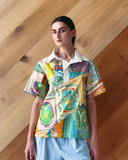 Model wearing patchwork Polo Top - mixed print shirt against a wooden wall.