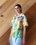 Model wearing patchwork Polo Top - mixed print shirt against a wooden wall.
