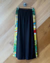 Black trousers with colourful patchwork hanging against a wooden wall.