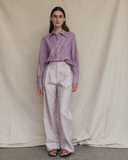 Woman wearing a plum striped shirt and high-waisted pink pants against a beige background