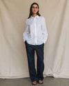 Model wearing a crisp white long-sleeve shirt with denim pants, against a canvas background.