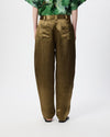 A person shown from the back wearing high-waisted, wide-leg trousers in a metallic olive-gold fabric, paired with a green patterned top and black sandals, against a plain white studio background.