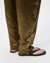 Close-up of a person's legs wearing wide-leg olive green trousers and black slide sandals against a plain white studio background.