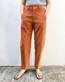 Person wearing rust-colored pants and a gray top against a white wall.