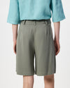 A person shown from the back wearing olive green tailored shorts and a light aqua blouse against a plain light gray studio background.