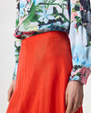 Model wearing a midi length orange skirt with patterned shirt and flip flops.