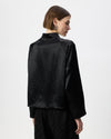 A model shown from the back wearing a black long-sleeve jacket and black trousers against a plain light gray studio background.