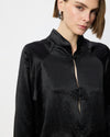 A close-up of a model wearing a black satin long-sleeve blouse with a mandarin collar and decorative flower-shaped buttons.