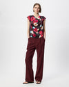 Model wearing a cowl draped top with a burgundy floral print paired with burgundy pants.