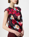 Model wearing a cowl draped top with a burgundy floral print with burgundy pants.