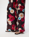 Wide-leg trousers with a dark floral print featuring red, cream, and light blue flowers, shown on a model wearing black slide sandals against a white studio background.