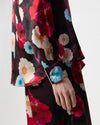 A close-up of a person wearing a long-sleeve floral shirt. The sleeve has a buttoned cuff with a decorative blue flower applique, and the model's hand is visible.