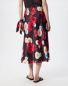 A model is shown from the back wearing a dark brown satin midi skirt with a vibrant red, pink, and white floral print, paired with black sandals against a plain white studio background.