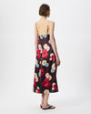 A woman viewed from the back wearing a sleeveless midi slip dress with thin straps and a dark floral print featuring red, pink, white, and light blue flowers on a black background.
