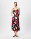 A model wearing a black midi slip dress with a vibrant red, pink, and white floral print, styled with black flip-flops against a plain white studio background.