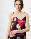 A woman wearing a dark floral satin slip dress with vibrant pink, red, and white flowers, photographed against a clean light gray studio background.