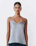 Woman wearing a light gray spaghetti strap top against a white background