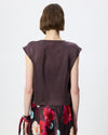 Model wearing a chocolate brown cowl draped top with a floral skirt against a white/grey studio background. 