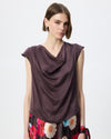 Model wearing a chocolate brown cowl draped top with a floral skirt against a white/grey studio background. 