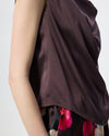 Model wearing a chocolate brown cowl draped top with a floral skirt against a white/grey studio background. 