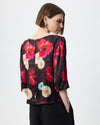Model wearing a dark burgundy patterned smock top with floral print and black trousers against a white/grey background. 