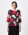 Model wearing a dark burgundy patterned smock top with floral print and black trousers against a white/grey background. 